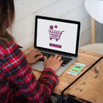 Online shopping website on laptop screen with female hands typin
